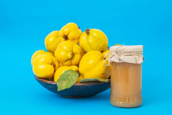 Quince fruit pile in a wooden bowl, with a jam jar without a label, soft focus close up isolated on blue background