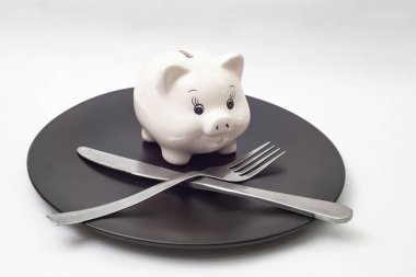 Siyah seramik tabakta gümüş çatal ve bıçakla beyaz, sevimli domuz kumbarası.