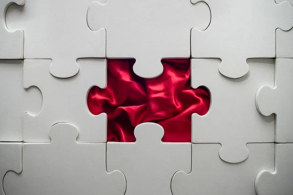 white jigsaw puzzle with a missing piece, and red satin folds