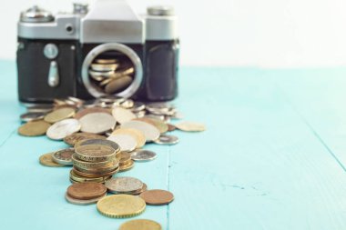 Defocused vintage camera with coins on the foreground, on blue background, soft focus close up