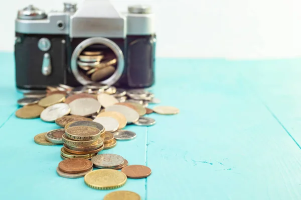 Defocused vintage camera with coins on the foreground, on blue background, soft focus close up