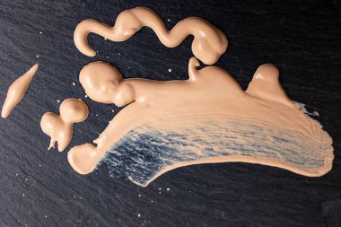 Liquid makeup splattered on black stone texture, macro