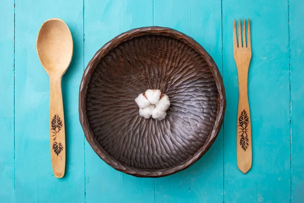 Wooden fork, spoon and sculpted bowl with a cotton flower, on acrylic  blue painted boards background.