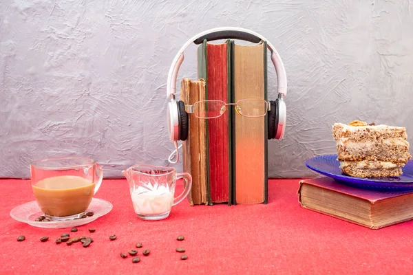 Study desk with red table cloth, coffee, cake, books, reading glasses and headphones