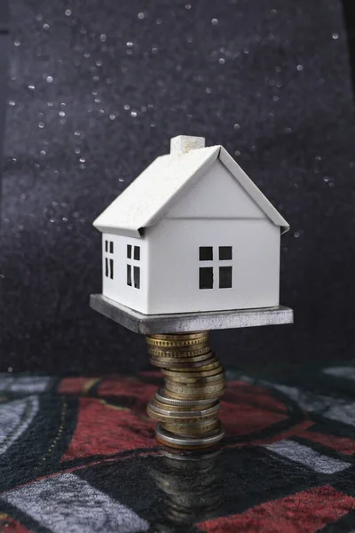 White model house on top of a stack of coins, on dark background , soft focus close up