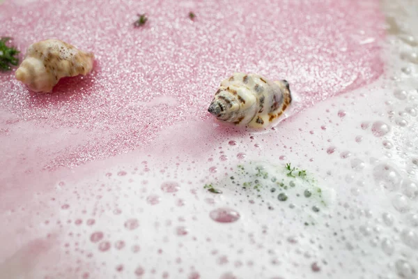 White foam, water and pink glitter with sea shells, abstract sea shore backdrop, soft focus close up
