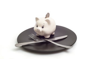 Gümüş çatal ve bıçaklı siyah seramik tabakta beyaz arka planda izole edilmiş, yumuşak odaklı, beyaz, sevimli domuz kumbarası.