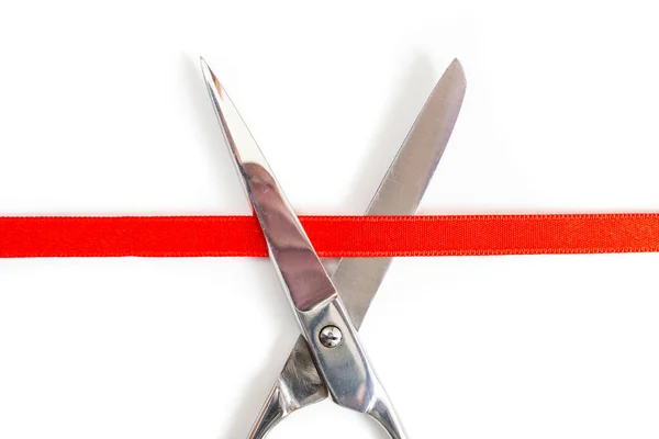 stock image Stainless steel scissors cutting a red satin ribbon, close up isolated on white