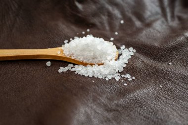 Tahta çay kaşığı beyaz kaya tuzu, kahverengi deri, deri dokusu, yumuşak odaklı soyut fon