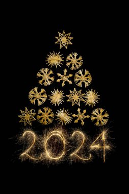 Saman kar taneleriyle yapılmış Noel ağacı üçgeni ve siyah arka planda izole edilmiş kıvılcımlarla yazılmış 2024 yeni yılı.