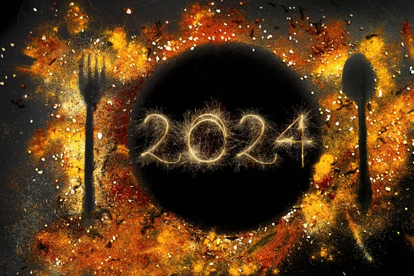Tabak silueti, kaşıkla çatal ve baharatlarla yapılmış koyu arkaplan. Kıvılcımlarla yazılmış 2024, yeni yıl partisi  