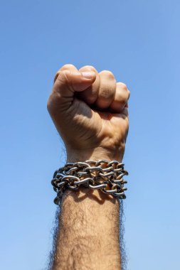 Kavrulmuş erkek yumruğu, bileğinde çelik zincir, mavi gökyüzüne karşı.  