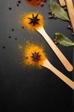 Paprika, zerdeçal ve defne yaprakları ahşap çay kaşıkları ve siyah arka plandaki çiçekler gibi sıralanmış.