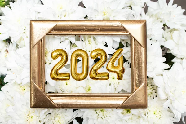 Golden frame and 2024 tin foil balloons on white chrysanthemum flowers background. new year festive