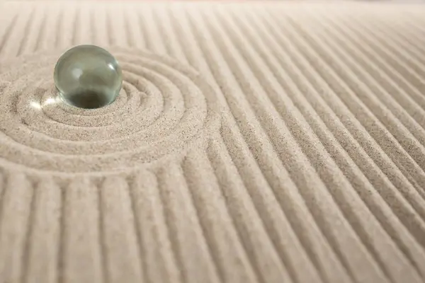 Miniature sand zen garden with a glass sphere and geometric dunes, abstract texture
