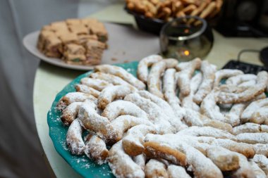 Yarım ay şeklinde kurabiyeler, üzerine pudra şekeri serpiştirilmiş yeşil bir tabakta, yumuşak bir odak noktası.  