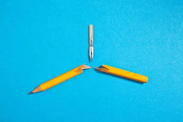 Vintage pen nib breaking a crayon in half, on blue paper background concept