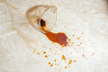 Şeffaf cam bardaktan dökülen kahve, mermer desenli masa arkaplanı, yumuşak odaklı.