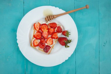 Peynirli, çilekli ve ballı ekmek dilimi, beyaz tabakta, mavi tahtalarda  