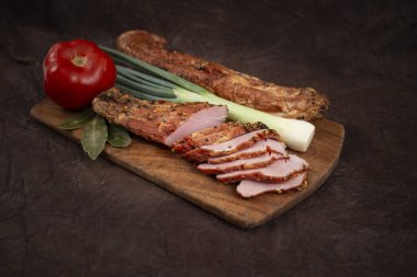 Domuz eti filetosu pastırması tütsülenmiş ve baharatlı, ince dilimlenmiş, domates ve taze soğanlı, ahşap kesme tahtasında, beyaz üzerine izole edilmiş.  