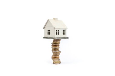 Beyaz arka planda izole edilmiş altın sikkelerin üzerinde duran minyatür metal ev.  