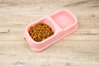Ahşap üzerinde kedi ya da köpek için kuru yiyecek ve su içeren pembe renkli plastik bir kap. 