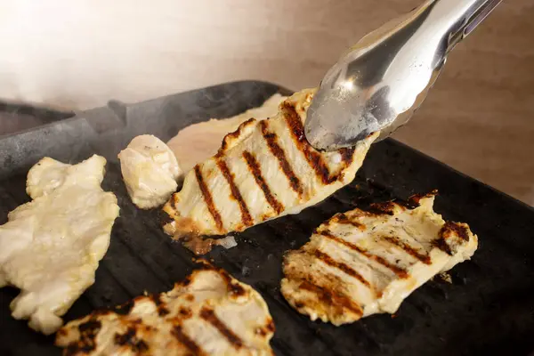 stock image Cooking chicken breast on a black cast iron grill ,using stainless steel tongs soft focus  