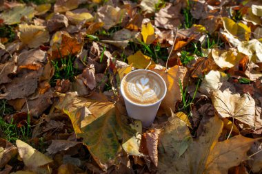 Altın sonbahar yapraklarıyla çevrili tek kullanımlık kağıt bardakta Latte sanatı.