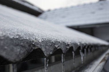 Dalgalanık bir çatıdan eriyen kar, küçük buz saçakları perspektifi, yumuşak odak  
