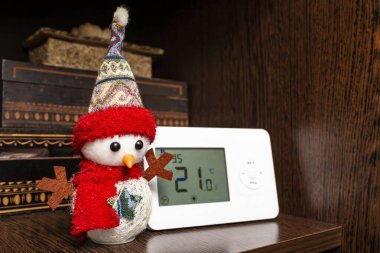 Snow man christmas decoration next to a wireless heating thermostat with 21 degrees on the display, soft focus  clipart