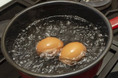 Two orange eggs boiling in a  black pot with bubbles and steam  clipart