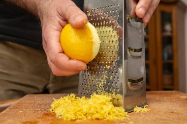 Erkek aşçı elleri paslanmaz çelik rendesinin üzerinde limon rendeleyen eller, limon aromalı, yumuşak odaklı aksiyon için.  