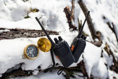 Donmuş beyaz karla kaplı ağaç kütüğündeki iki siyah telsiz altın bir pusulanın yanında, dağ gezisi.  