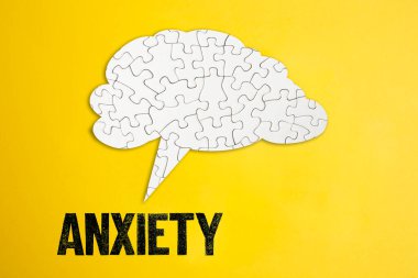Yapboz yap-boz beyin şekli konuşma balonu sarı karton arka planda anksiyete sözcüğü yazılı  