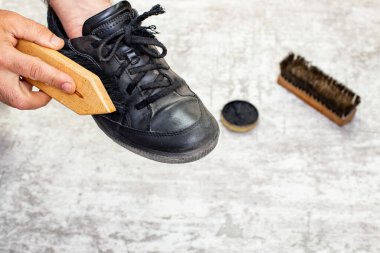 Erkek el, siyah krem ve gri üzerinde ahşap bir fırça ile spor deri ayakkabı cilalıyor.  