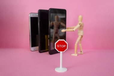 Ahşap manken pembe arka planda akıllı telefonları kucaklıyor, dur işareti ve minyatür bir selfie çekiyor.  
