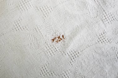 Beyaz desenli beyaz kumaş masa örtüsünde yırtılmış bir delik.