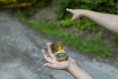 Erkek çocuk ormanda altın bir pusula tutuyor ve işaret parmağıyla yolu gösteriyor. Yavaşça odaklan.  