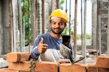 Mutlu gülümseyen genç Hintli inşaat işçisi iş yerinde cep telefonuyla meşgul.