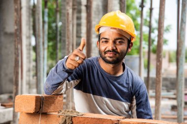 Kendine güvenen Hintli erkek inşaat işçisi, şantiyede çalışırken onay ya da zafer işareti gösteriyor