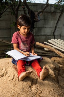 Annesi çalışırken küçük Hintli inşaat işçisi kız çocuğu okuyor.