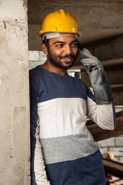 Mutlu gülümseyen genç Hintli inşaat işçisi iş yerinde cep telefonuyla meşgul.