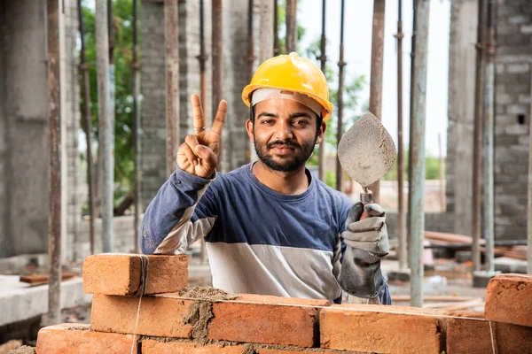 stock image confident Indian male Construction worker showing thumbs-up or victory sign while working at site