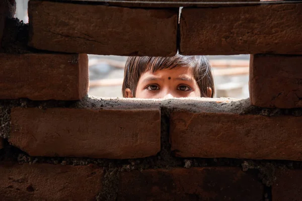 An Indian labour girl child looking  through under construction brick wall window