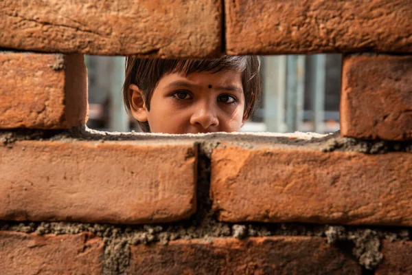 An Indian labour girl child looking  through under construction brick wall window