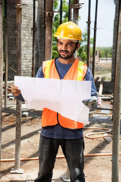 Indian man or asian construction worker holding roll paper of drawing Structural plan at site