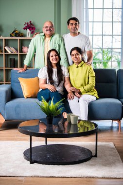 Modern evdeki oturma odasında grup fotoğrafı için poz veren dört kişilik Hintli aile.