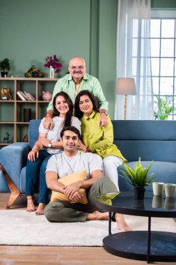 Modern evdeki oturma odasında grup fotoğrafı için poz veren dört kişilik Hintli aile.