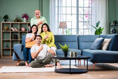 Mutlu ve güzel bir aile kanepede oturuyor ve sollarını işaret ediyor.