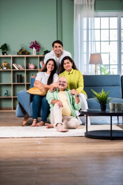 Modern evdeki oturma odasında grup fotoğrafı için poz veren dört kişilik Hintli aile.